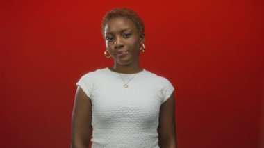 Kırmızı stüdyoda kalp kolyesi takan genç bir kadın parmağıyla işaret ediyor; davet yaklaşım bağlantısı.