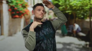 Genç bir adam canlı bir şehir caddesinde ağaçlar ve arka planda insanlar olan çerçeveli bir jest yapıyor, canlı bir çevrede yaratıcı bir ifade ortaya koyuyor..