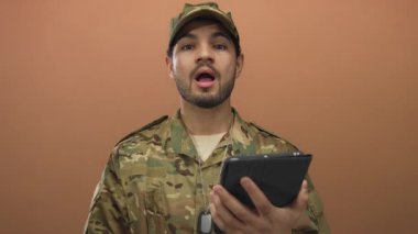 Kamuflaj üniformalı adam tablet cihazını tutuyor ve stüdyoda kameraya bakıyor. Kararlılık odaklı..