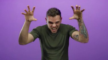 Dövmeleri olan, gülümseyen ve neşeli poz veren genç bir adam canlı mor bir arka planı, dövmeli kolları ve yeşil gömleği var..