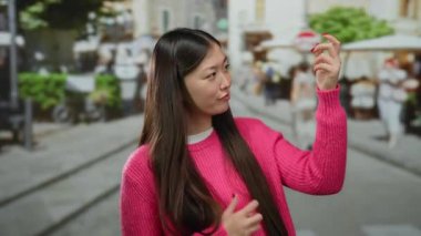 Şehir sokaklarında canlı şehir arkaplanı olan canlı pembe süveterle gitar çalan kadın taklidi yapıyor..