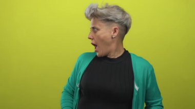 Stüdyoda kısa gri saçlı, siyah bluzlu ve yeşil hırkalı bir kadın açık elle omuz silkiyor. Sürpriz!.