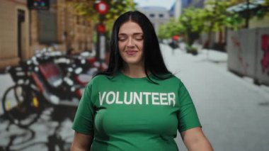 Yeşil tişörtlü gönüllü kadın şehir sokaklarında bisiklet arka planı bulanık, pozitiflik ve açık hava ortamında toplum ruhunu gösteren jest yapıyor..