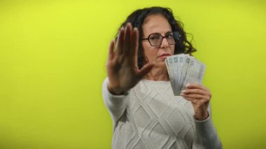 Orta yaşlı kadın Mısır kilosu tutuyor ve jestler canlı sarı duvara karşı duruyor, dinamik bir sahne yaratıyor..