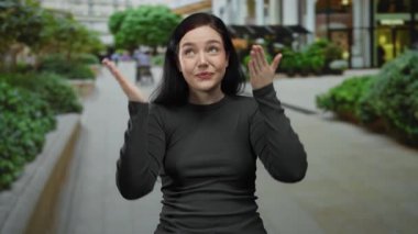 Esmer kadın bir şehir sokak dekorunda neşe içinde gözleri kaplayan, şehir yeşilliği ve açık binalar arasında şaşırmış görünüyor.