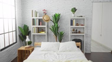 Stüdyoda yumuşak güneş ışığı altında yatakta dans eden kadın kitaplıklar ve bitkilerle; neşe dinginliği.