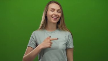 Gülümseyen ve işaret eden bir kadın canlı yeşil izole bir arka plan karşısında, pozitiflik ve güven yayarak, günlük tarzını ve anlamlı jestini vurguluyor..