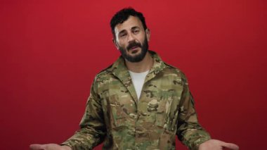 Kırmızı arka planda askeri üniformalı İspanyol sakallı bir adam gururlu ve otoriter bir şekilde kameraya bakıyor.