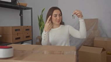 Genç sarışın kadın yeni evdeki anahtarları işaret ediyor. İçinde taşınan kutular ve raflar var. Kapalı mekanında yeni bir başlangıç yapıyor..