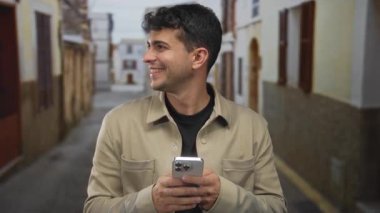 Köy sokaklarında akıllı telefonu olan İspanyol adam gülümsüyor; eğlence bağlantısı.