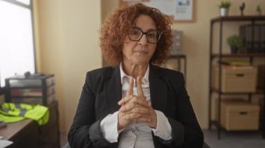 Ofis ortamında düşünen, gözlüklü ve takım elbiseli, düşünceli bir ifadeyle düşünceli bir kadın, içeride düşüncenin ve profesyonelliğin özünü vurguluyor..