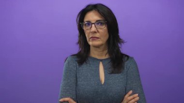 Mor stüdyoda ciddi bir ifade ve kollarını kavuşturmuş gözlüklü İspanyol bir orta yaşlı kadın..