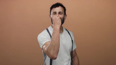 Sakallı İspanyol bir adam turuncu arka plana karşı şefin öpücüğünü yapıyor. Beyaz gömlek ve pantolon askısıyla kendine güveni ve tarzı var..