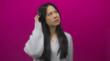 Çinli bir kadın canlı pembe arka plana karşı düşünceli bir ifade sergiliyor modern moda ve derin yansımayı vurgulayan izole bir ortamda düşünceli bir ifade sergiliyor.