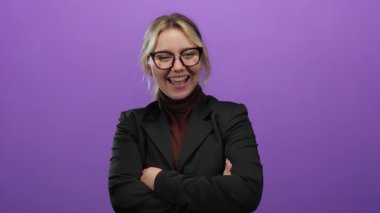 Siyah takım elbiseli, mor bir arka plan karşısında kolları çaprazlanmış, güvenle gülümseyen bir kadın..