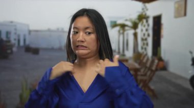 Şehir merkezinde açık havada mavi gömlekli bir kadın gündüz vakti sinirli bir ifade sergiliyor. Açık hava ortamında genç kadın enerjisini somutlaştırıyor..