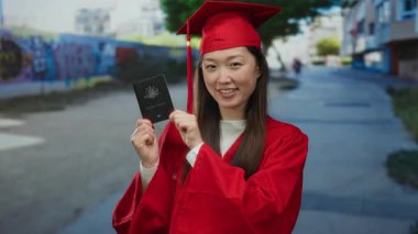 Kırmızı mezuniyet elbisesi giymiş bir kadın Avustralya pasaportunu şehir caddesinde gururla sergiliyor..