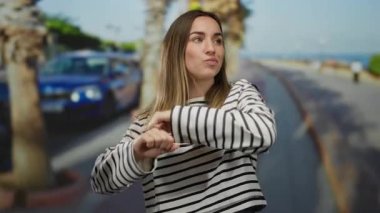 Güneşli bir sokakta mutlu bir şekilde dans eden bir kadın. Üstü çizgili. Arka planda bulanık arabalar ve palmiye ağaçları olan açık havada neşe ve özgürlüğü ifade ediyor..