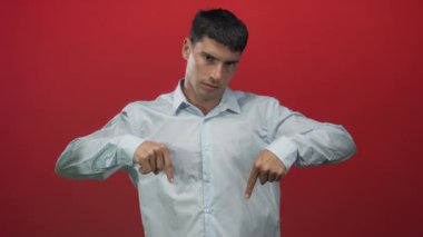 Açık mavi gömlekli adam kırmızı stüdyo ortamında işaret parmağı aşağı doğru; ciddi öneri.