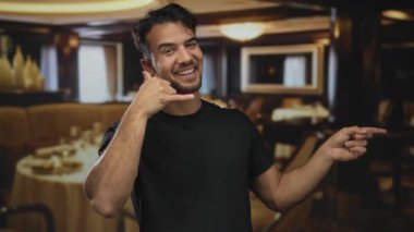 Genç İspanyol bir adam hoş bir restoranda hoş bir jest yapıyor ve gülümsüyor. Zarif bir dekor ve ortam aydınlatmasıyla, dostane ve canlı bir atmosfer yayıyor..