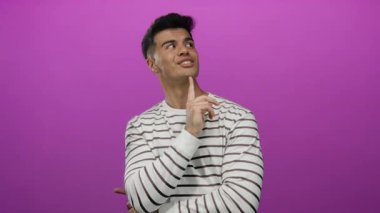 Genç, ispanyol, elleri çenesinde çizgili tişört giyen soyutlanmış, pembe arka planda tefekkür ve karar verme mekanizmasını gösteren bir adam..