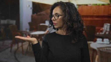 Orta yaşlı İspanyol kadın avucunu açıyor ve açık kafe terasında el hareketi gösteriyor; reddetme inkar.