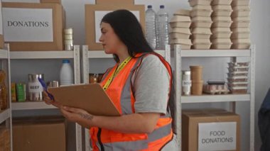 Bağış toplayan bir kadın, gıda malzemelerinin arasında gönüllü yelek giyiyor, organizasyonu ve toplum desteğini resmediyor..