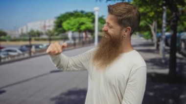 Uzun sakallı, uzun boylu, güneşli caddede uzanan elleri olan beyaz bir genç adam..