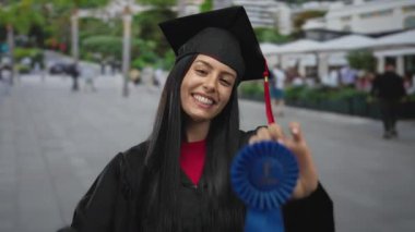 Mezuniyet üniformalı İspanyol kadın, şehir sokaklarında mavi kurdeleyle gururla geziyor. Şehir ortamının başarısını ve başarısını simgeliyor..