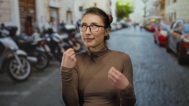 Parlak şehir ortamında, parlayan bir kaldırım taşı caddesinde gözlüklü genç bir kadın, park etmiş motosikletler ve parlak gün ışığında arabalarla çevrili..