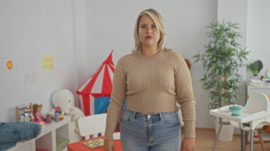 Kırmızı oyun çadırının yanında duran çapraz kollu kadın ve anaokulunda öğrenme masası; kendine güven..