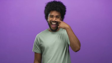 Burnunu gösteren gözlüklü gülümseyen bir adam canlı mor bir arka plana karşı poz veriyor, izole edilmiş bir stüdyoda neşeli ve kendinden emin bir ruh hali sergiliyor..