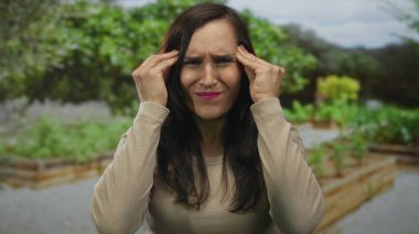 Güneşli bir günde canlı bir yeşil park ortamında hayal kırıklığını ifade eden bir kadın, yemyeşil yeşilliklerle çevrili, duygularını ve açık hava ortamını vurgulayan..