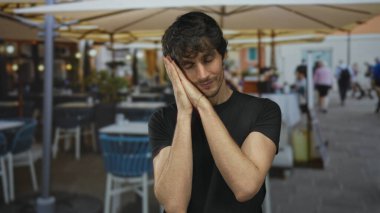 Genç adam öğle vakti güneş şemsiyesi altında, restoran terasında kollarını açarak ellerini çırpıyor; sakin bir uyku uykusunda.