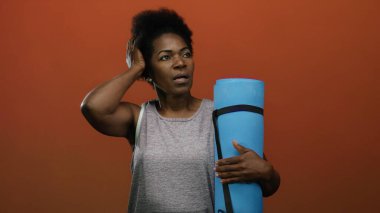 Yoga minderli kadın kırmızı arka planda dikiliyor. Eli başının üstünde duruyor. Düşünceli bir anı işaret ediyor..