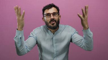 Sakallı İspanyol bir adam pembe bir arka plana kafa karışıklığı gösteriyor, gözlük takıyor ve mavi gömlek giyiyor, dramatik hayal kırıklığı ve şaşkınlık hareketleri sergiliyor..