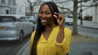 Kıvırcık saçlı gülümseyen kadın şehir sokaklarında jest yapıyor. Bulanık şehir arkaplanıyla neşeli ve neşeli bir atmosfer sergiliyor..