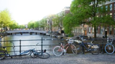 Amsterdam, Hollanda 'da bir kanal boyunca park etmiş bisikletlerin bulanık görüntüsü. Ağaçlar ve binalar arka planda bokeh etkisi yaratıyor..