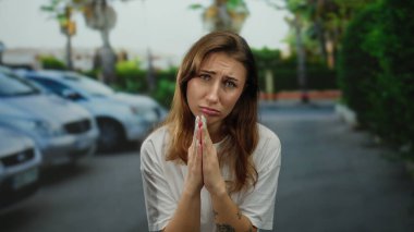 Dövmeli ve manikürlü bir kadın, arka planda arabaları olan bir şehir sokağında hüzünlü bir ifadeyle yalvarıyor. Duygularını ve şehir hayatını aktarıyor..