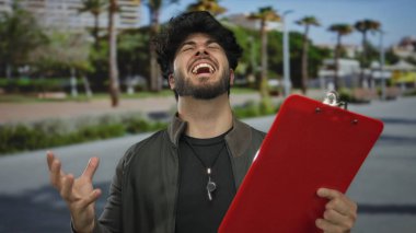 Sakallı genç adam, arka planda bulanık şehir manzarası olan ve güneşli şehir sokaklarında merakla ve dikkatle kırmızı panoyu inceliyor..