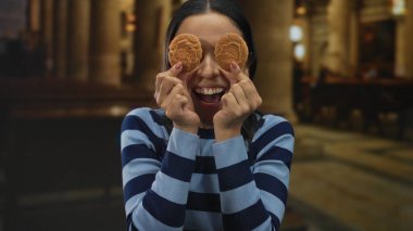 Kilisede neşeli bir şekilde gülümseyen kadın gözlerinde kurabiyeler tutuyor, eğlenceli ve neşeli bir atmosfer yaratıyor..