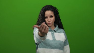 Yeşil arka plana karşı davetkar bir jest yapan, çizgili süveter giyen, iletişimi ifade eden, İspanyol kökenli, canlı bir ortamda izole edilmiş, genç görünümlü bir kadın..