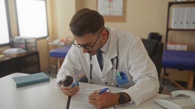 Elinde ilaç şişesi olan ve parlak bir klinik danışma odasında steteskop takan bir adam..