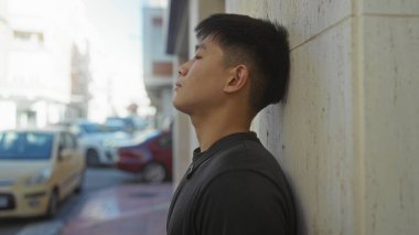 Şehir sokaklarında duvara yaslanan genç adam, hareketli şehir ortamında huzurlu bir açık hava anını yakalıyor..