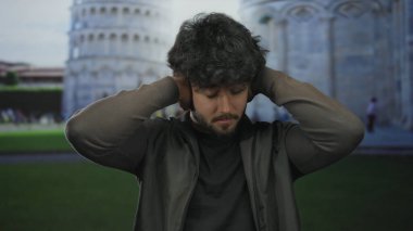 Sakallı genç adam güneşli bir günde sidik kulesinin önünde kulaklarını kapatıyor İtalya 'da bir ifade anı yakalıyor..