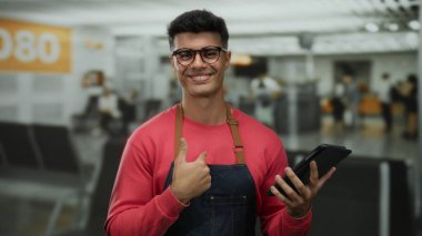 Yoğun havaalanı terminalinde önlüklü genç bir adam. İçerde güvenle gülümseyerek çekici bir şekilde poz veriyor..