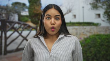 Genç İspanyol bir kadın, güneşli bir günde yeşil bir bahçede komik bir yüz ifadesi takınıyor ve ağaçlar onu kuşatmış..