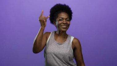 Kadın, güven ve ifadeyi vurgulayan münferit mor arka plana gülümserken kaya hareketi yapıyor.