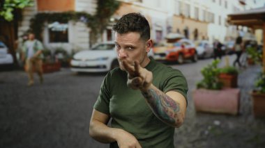Canlı bir şehir caddesinde hareketli bir jest yapan İspanyol dövmeli genç adam, hareketli şehir hayatı arasındaki gözlem ve farkındalığı vurguluyor..
