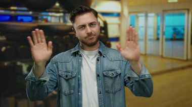 Sıradan kot ceketli sakallı genç adam spor salonunda arka planda bulanık spor ekipmanlarıyla fitness ortamını öneriyor.